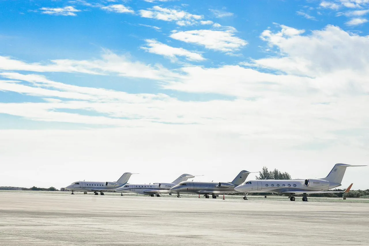 A fleet of luxury private jets lined up on the runway under a blue sky